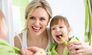 Mama uczy córkę, jak myć zęby niemowlakowi. Uśmiechnięte twarze i zielone szczoteczki.
