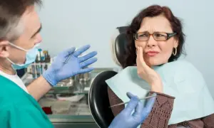 Kobieta z bólem zęba u dentysty, który pokazuje narzędzia. Wygląda na to, że czeka ją leczenie zatrucia zęba.