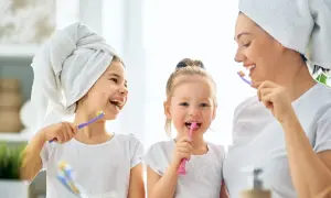 Mama z córkami myje zęby. Od kiedy myć zęby dziecku? Od pierwszego ząbka! Uśmiechnięte buzie i szczoteczki w rękach.