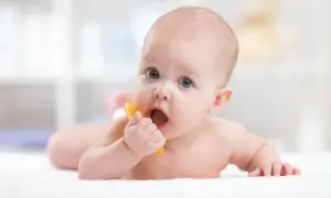 Niemowlę z niebieskimi oczami gryzie pomarańczową zabawkę. Czy późne ząbkowanie a inteligencja to mit?