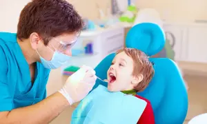 Dentysta bada uśmiechniętego chłopca, sprawdzając, ile zębów ma roczne dziecko.