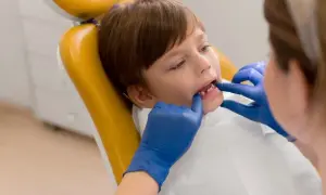 Chłopiec na żółtym fotelu dentystycznym, u którego lekarz w niebieskich rękawiczkach bada zęby, by wykluczyć choroby dziąseł u dzieci.