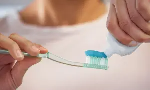 Nakładanie niebieskiej pasty do zębów z fluorkiem cyny na szczoteczkę.