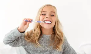 Uśmiechnięta dziewczynka z blond włosami myje zęby. To świetny sposób, jak zachęcić dziecko do mycia zębów, gdy jest to przyjemne!