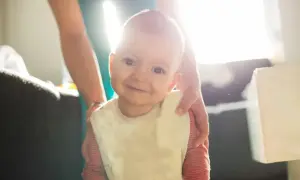 Uśmiechnięte dziecko w śliniaczku, z kropelkami śliny na brodzie. To normalne, dlaczego dziecko się ślini, gdy rosną mu ząbki.
