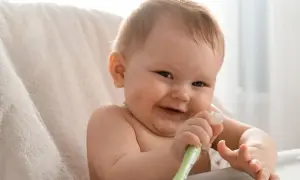 Uśmiechnięte niemowlę bawi się swoją pierwszą szczoteczką do zębów dla niemowląt, odkrywając higienę jamy ustnej.