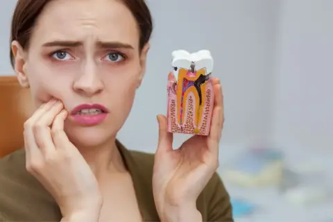 Kobieta z bólem zęba trzyma model z widoczną czarną kropką na plombie, wskazującą na próchnicę.