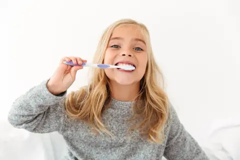 Uśmiechnięta dziewczynka z blond włosami myje zęby. To świetny sposób, jak zachęcić dziecko do mycia zębów, gdy jest to przyjemne!