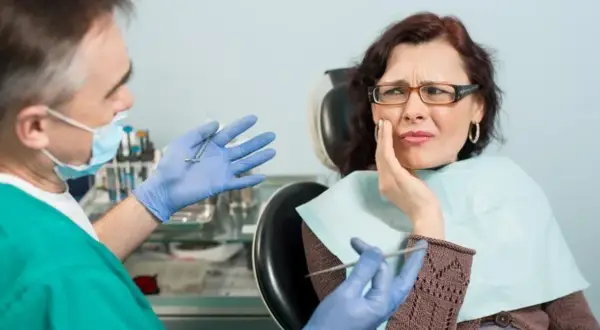 Kobieta z bólem zęba u dentysty, który pokazuje narzędzia. Wygląda na to, że czeka ją leczenie zatrucia zęba.