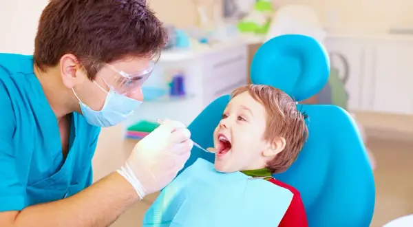 Dentysta bada uśmiechniętego chłopca, sprawdzając, ile zębów ma roczne dziecko.
