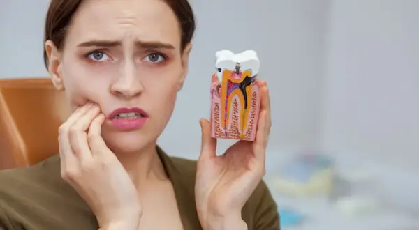 Kobieta z bólem zęba trzyma model z widoczną czarną kropką na plombie, wskazującą na próchnicę.