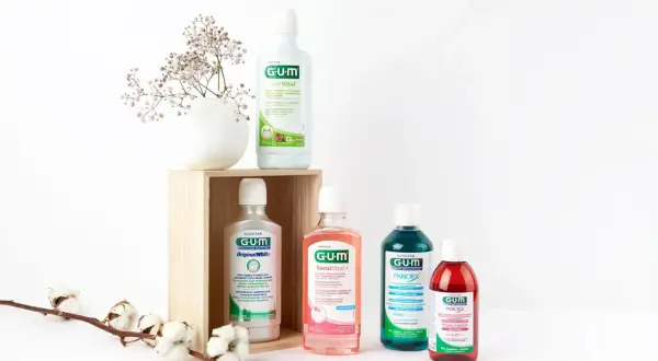 Wybierasz, czym płukać dziąsła? Cztery płyny GUM: ActiVital, Original White, SensiVital+ i Paroex, obok delikatnych kwiatów, sugerują różne opcje pielęgnacji.
