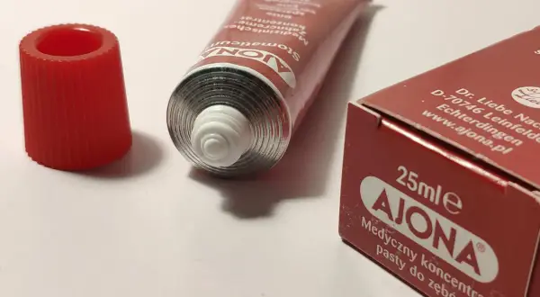 Pasta Ajona, medyczny koncentrat do zębów. Zastanawiasz się nad jej stosowaniem i potencjalnymi skutkami ubocznymi? Tubka i opakowanie na białym tle.