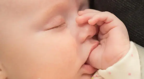Słodki noworodek śpi, a jego mała rączka delikatnie obejmuje usta. To urocze ssanie kciuka u noworodka uspokaja go.