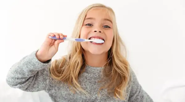 Uśmiechnięta dziewczynka z blond włosami myje zęby. To świetny sposób, jak zachęcić dziecko do mycia zębów, gdy jest to przyjemne!