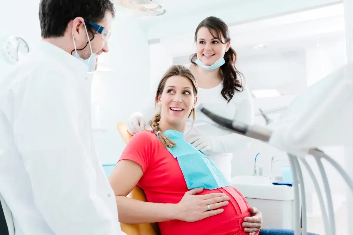 Uśmiechnięta ciężarna pacjentka u dentysty. Lekarz i asystentka dbają o jej zdrowie, zapewniając komfort podczas wizyty.