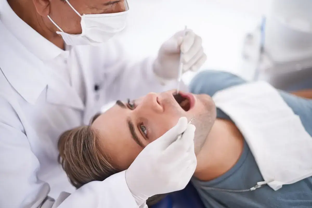 Dentysta bada jamę ustną pacjenta, szukając zmian. Lekarz stomatolog używa narzędzi do dokładnego oglądania.