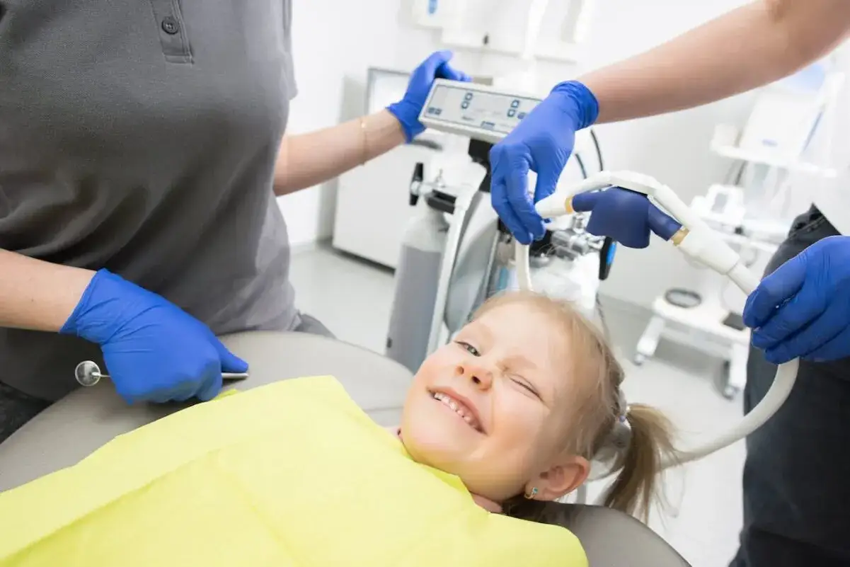 Uśmiechnięta dziewczynka na fotelu dentystycznym, z uśmiechem, kt&oacute;ry może sugerować lekkie krzywe zęby u dziecka.