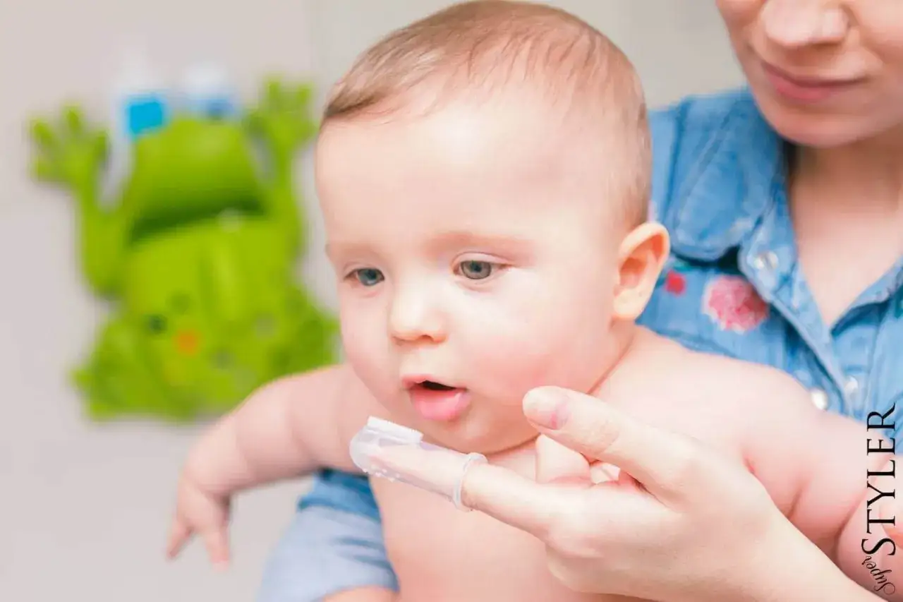 Mama pokazuje dziecku, od kiedy myć zęby dziecku, używając specjalnej nakładki na palec.