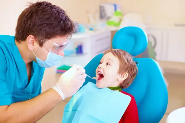 Dentysta bada uśmiechniętego chłopca, sprawdzając, ile zębów ma roczne dziecko.
