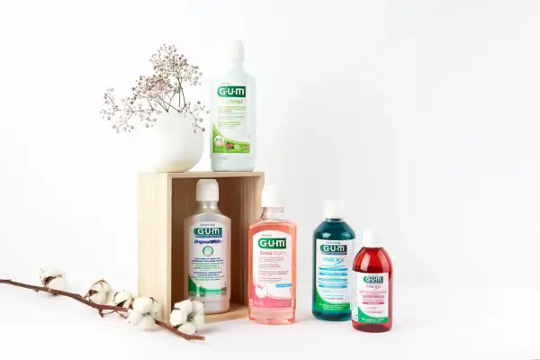 Wybierasz, czym płukać dziąsła? Cztery płyny GUM: ActiVital, Original White, SensiVital+ i Paroex, obok delikatnych kwiatów, sugerują różne opcje pielęgnacji.
