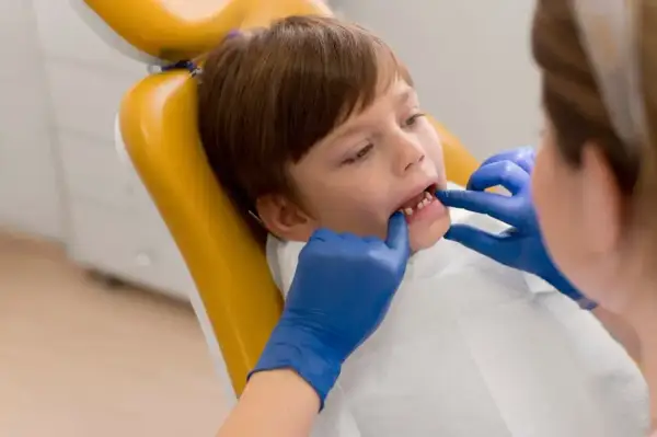Chłopiec na żółtym fotelu dentystycznym, u którego lekarz w niebieskich rękawiczkach bada zęby, by wykluczyć choroby dziąseł u dzieci.
