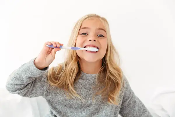 Uśmiechnięta dziewczynka z blond włosami myje zęby. To świetny sposób, jak zachęcić dziecko do mycia zębów, gdy jest to przyjemne!